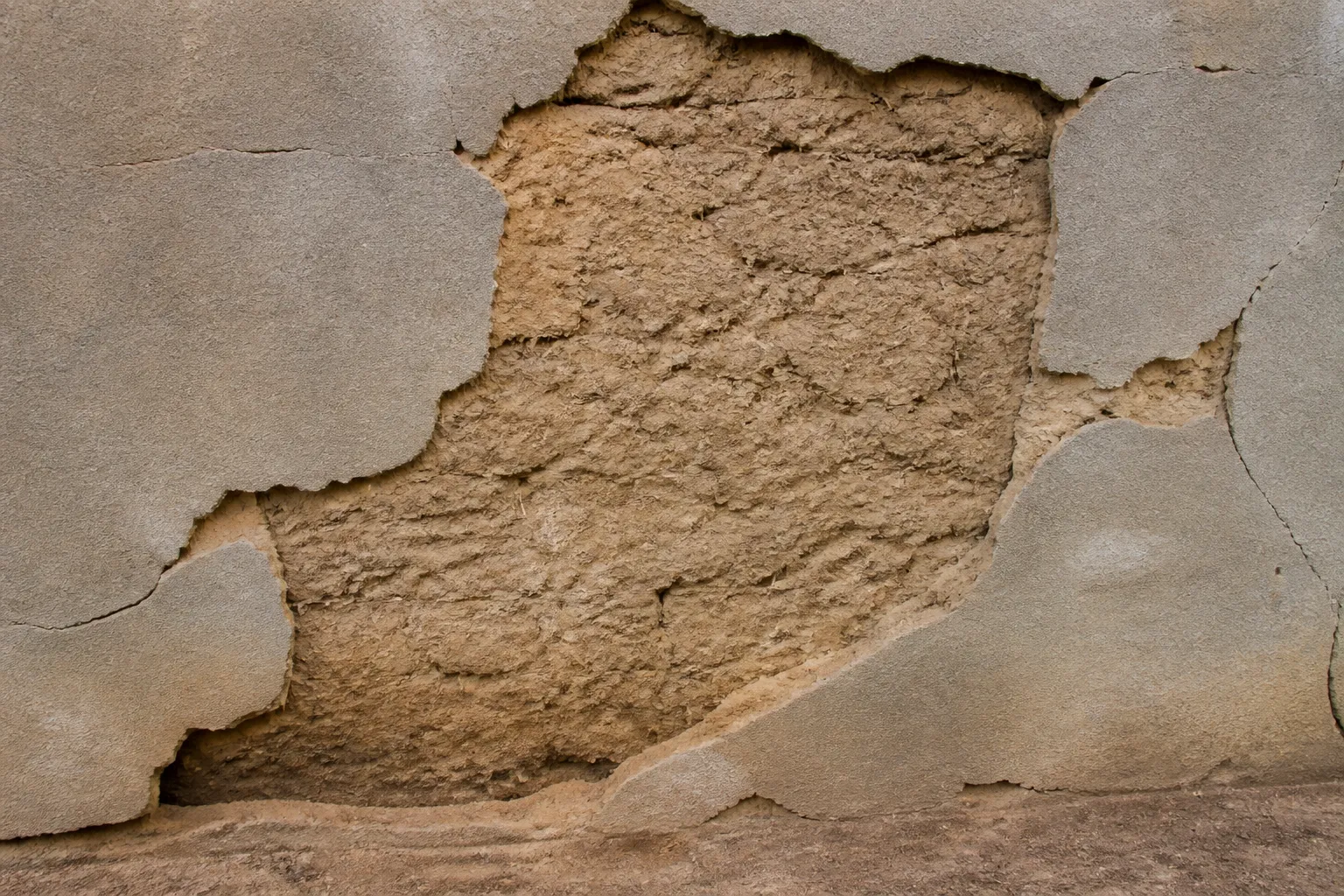 Enduit ciment decolle sur un mur en terre crue